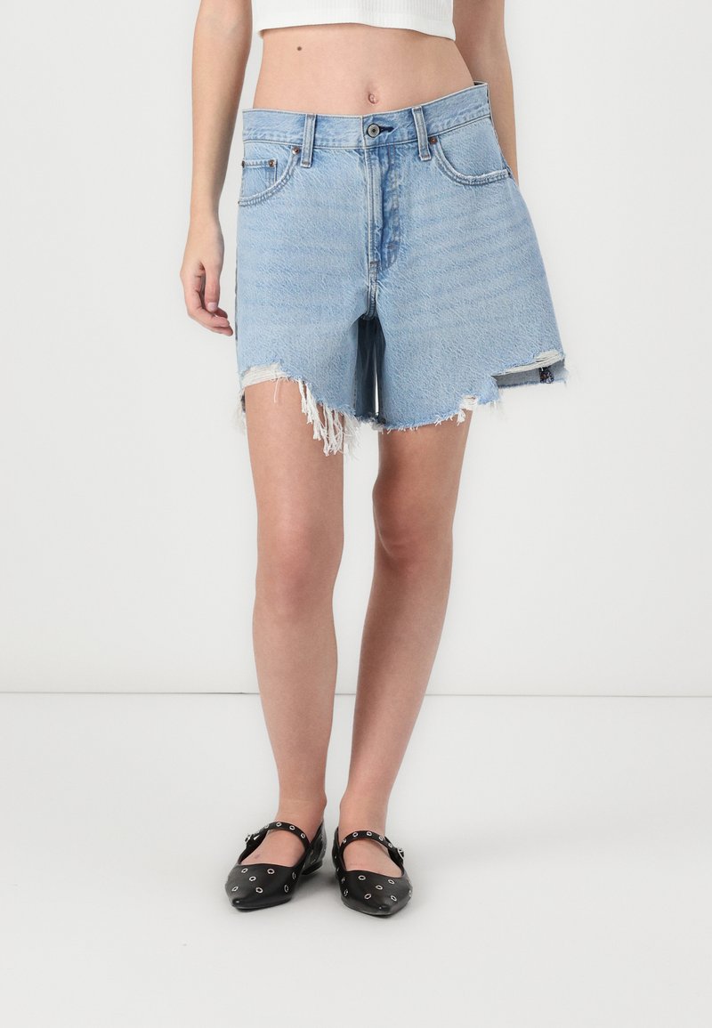 Lichtblauwe denimshorts met een versleten zoom en rafelige randen. G gedragen met zwarte flats en een aansluitend wit crop top.
