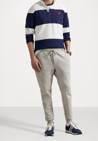 Marinblå och vit randig långärmad polo med röd brodyr, tillsammans med ljusgrå sweatpants och blåa träningsskor.