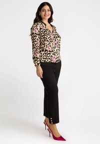 Blusa a stampa leopardata in beige con accenti neri e rosa, abbinata a pantaloni neri con dettagli in bottone dorato all'orlo, e tacchi rosa.