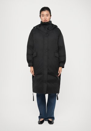 Cappotto lungo imbottito nero con colletto alto, chiusura frontale con bottoni e due tasche laterali. Presenta stringhe al fondo e ai polsini.