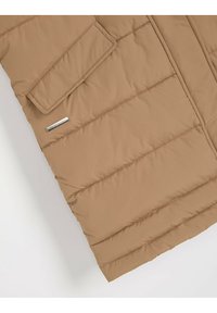 Brązowa kurtka ocieplana z prostokątną kieszenią klapową, ukośnym wzorem pikowania oraz metalową metką marki z przodu.