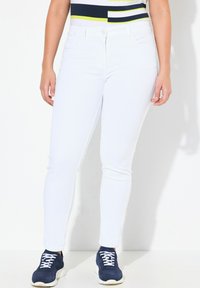 Jeans blancos ajustados con una textura suave, que presentan un diseño clásico de cinco bolsillos y una cinturilla de altura media. Combinados con zapatillas de deporte azul marino.
