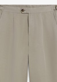 Pantalones beige de cintura alta con cierre de botón y cremallera, bolsillos laterales, pliegues y una hebilla lateral ajustable en la cintura.