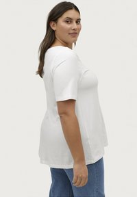 Hvid bomulds T-shirt med rund halsudskæring og korte ærmer, der har en løstsiddende pasform og en lige kant. Sammen med denim jeans.