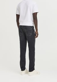Jeans de mezclilla negra con corte recto, que cuentan con dos bolsillos traseros, costuras blancas y detalles desgastados. Combinados con una camiseta blanca básica.