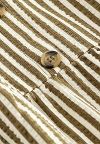 Gros plan d’un tissu texturé rayé marron et blanc avec un bouton rond bicolore marron cousu dessus.