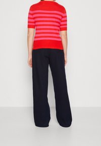 Punainen ja vaaleanpunainen raidallinen lyhythihainen paita, yhdistettynä löysiin tummansinisiin housuihin. Silkkinen rakenne, pyöreä kaula-aukko ja ribbireunus.