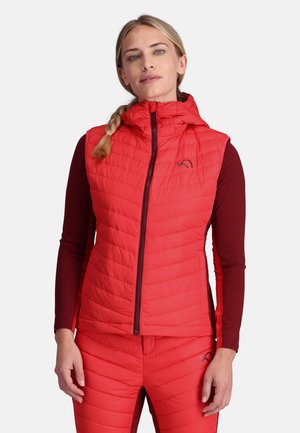 Punainen eristetty liivi hupulla, jossa on tilkkutyylinen muotoilu, vetoketjusuljenta ja rintaosassa logo. Päällä pitkähihaisen paidan. 