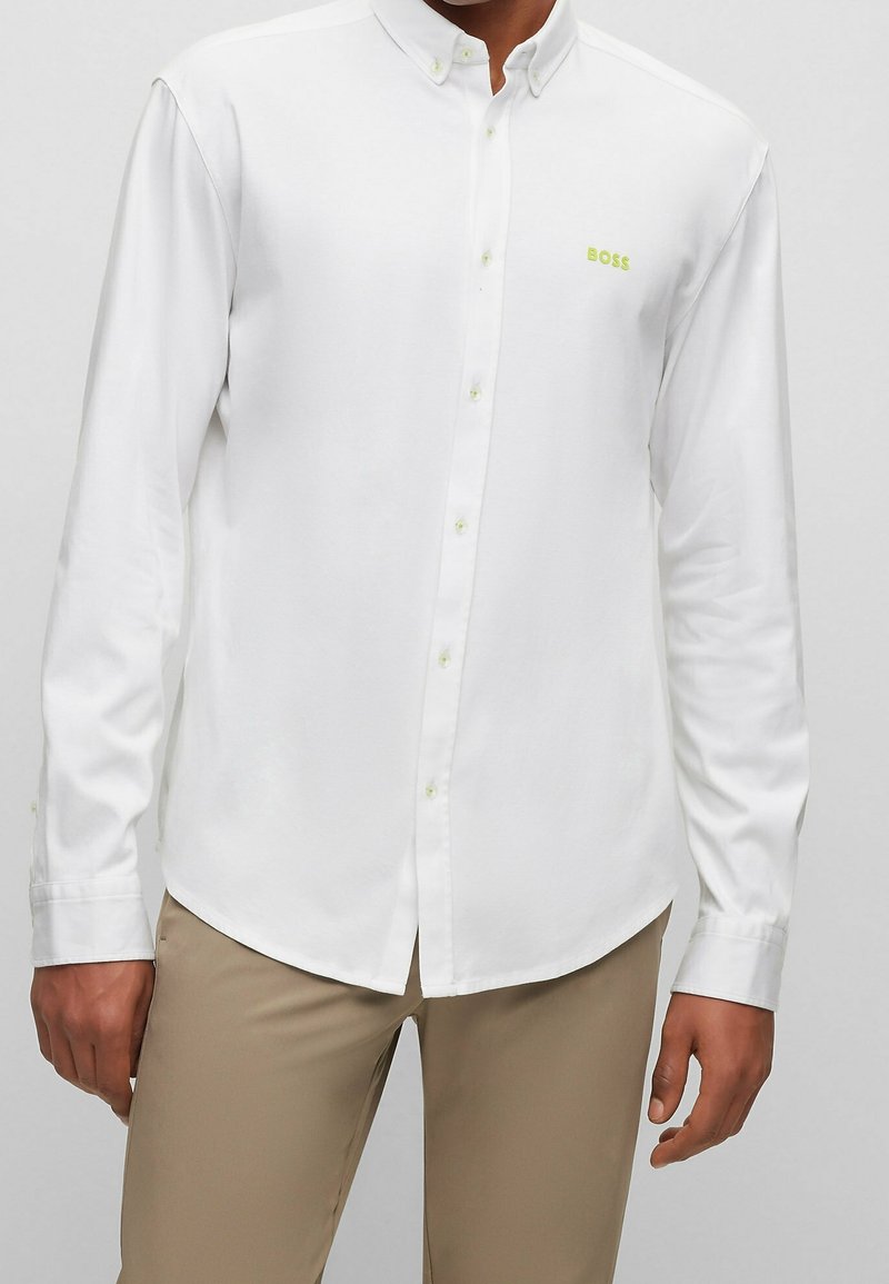 Camicia bianca button-up con maniche lunghe, logo verde chiaro sul petto e bottoni verde chiaro. Tessuto liscio e design del colletto classico.