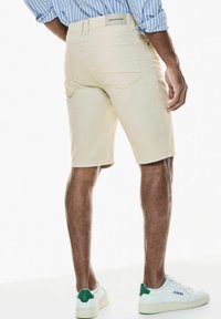 Svetlé béžové šortky z denimu s dvěma zadními kapsami a hladkým povrchem, doplněné bílými botami s zelenými akcenty.