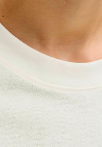 Lichtgekleurde gebreide stof met een geribbelde ronde halslijn en een subtiele textuur en stiksel langs de kraag.