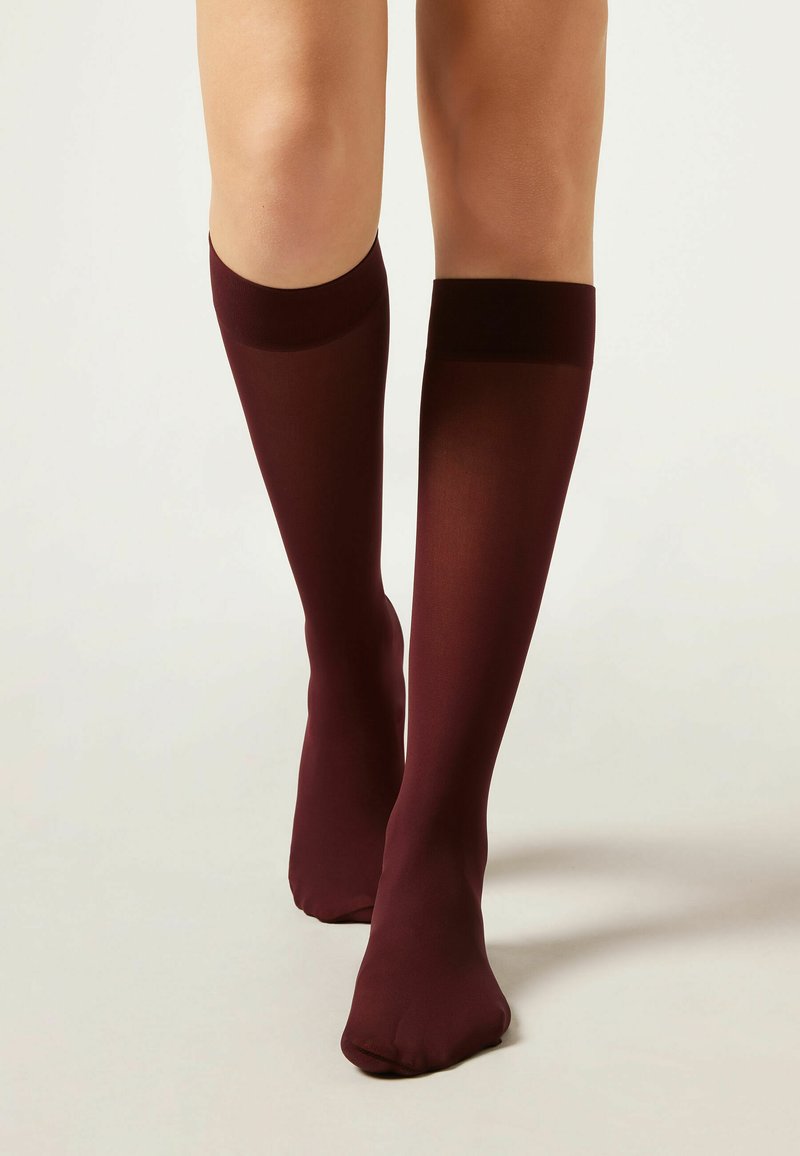 Burgundy knästrumpor av genomskinligt material med en mjuk yta. Har en solid kant högst upp och en sömlös fotdesign.