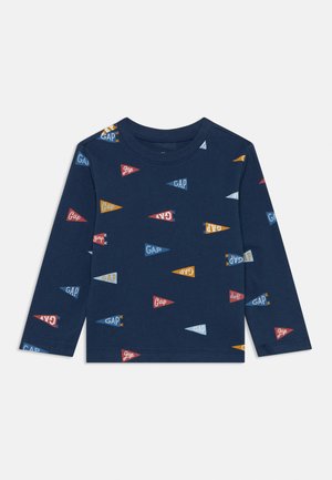 Camisa de manga longa azul-marinho com uma mistura de pequenos padrões de bandeirinhas coloridas apresentando a palavra "GAP" em várias cores e orientações.