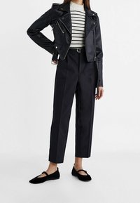 Veste de motard en cuir noir, pull blanc à rayures, pantalon noir taille haute et ballerines noires à bride. Matériaux texturés, coupe ajustée.