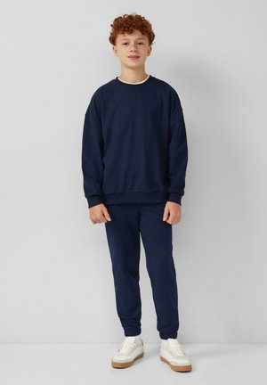 Marineblauw katoenen sweatshirt en bijpassende joggers met elastische boorden, gecombineerd met witte sneakers met een gummizool. Eenvoudig, casual ontwerp.