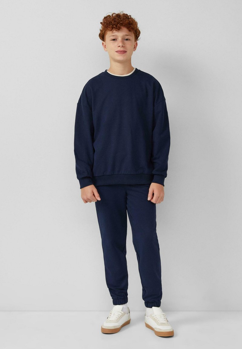 Marineblauw katoenen sweatshirt en bijpassende joggers met elastische boorden, gecombineerd met witte sneakers met een gummizool. Eenvoudig, casual ontwerp.