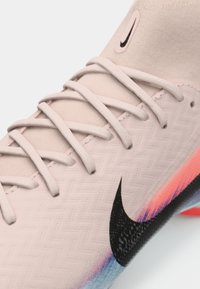 Κοντινή λήψη ροζ αθλητικού παπουτσιού Nike με λευκές κορδόνες, μαύρο λογότυπο swoosh και σόλα με gradation χρωμάτων σε μπλε, μωβ και πορτοκαλί.