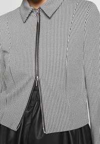 Veste courte ajustée à motif pied-de-poule noir et blanc. Elle présente une fermeture éclair et un col classique, avec un tissu texturé.