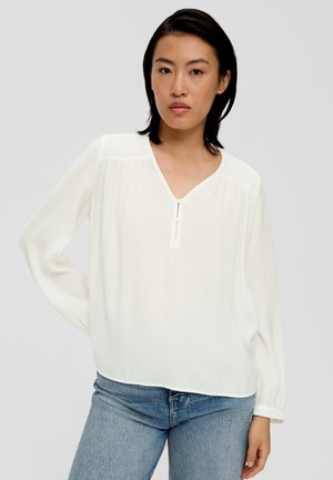 Blouse blanche à manches longues en tissu léger. Présente un col en V avec une fermeture à boutons discrète et des détails froncés aux épaules.
