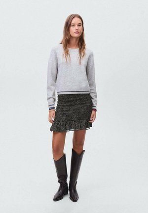 Maglione grigio con maniche lunghe e orlo a righe, abbinato a una gonna nera floreale con arricciature e un bordo arricciato, e stivali neri al ginocchio.