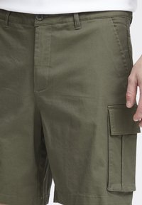 Olivengrønne cargo shorts lavet af bomuld, med knaplukning, sidelommer og en laplomme på højre ben. Glat tekstur.