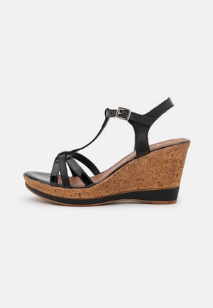 Black patent leather wedge sandals with cork platform, featuring a T-strap design and adjustable ankle buckle, smooth finish, and textured wedge.