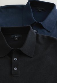 Två polo-skjortor: en marinblå med texturerad tyg och krage med knäppning; en solid svart i slätt tyg med krage med knäppning, båda märkta "NEXT."