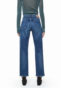 Vaqueros de pierna ancha de mezclilla en azul, con cintura alta, dos bolsillos traseros y bajos sin rematar, combinados con una camiseta ajustada de manga larga y brillante.