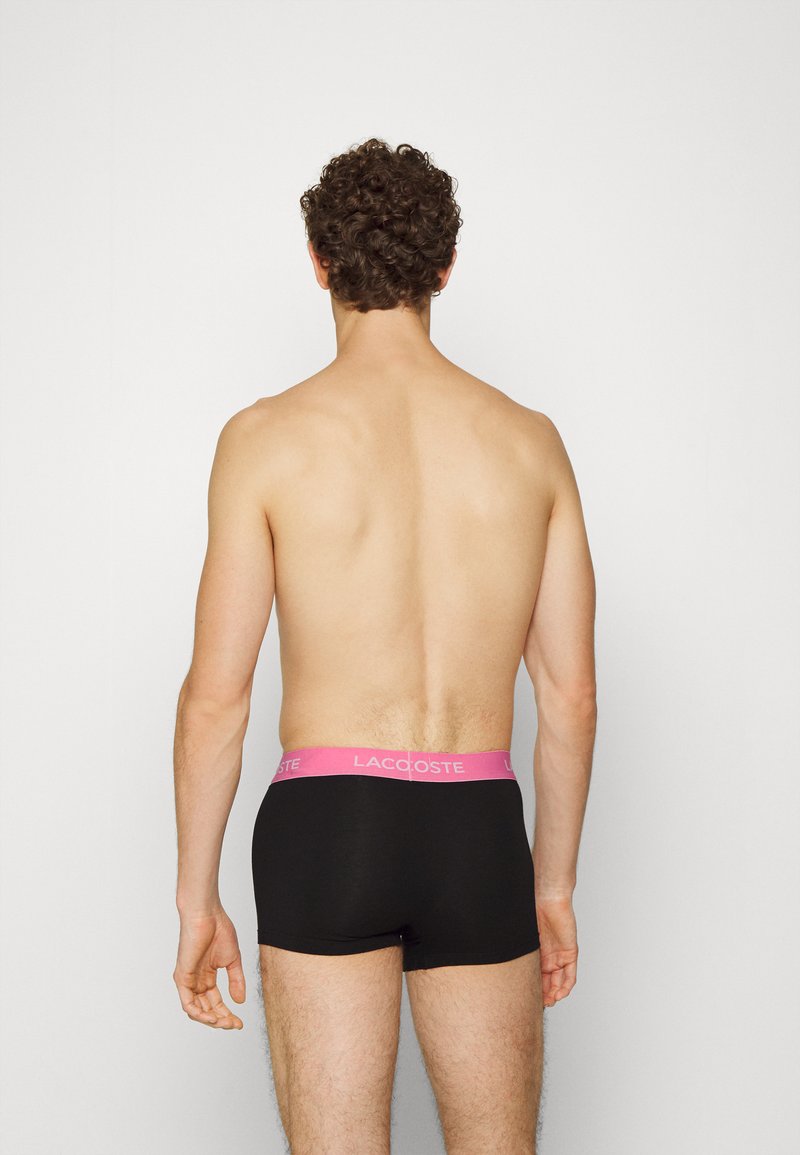 Zwarte boxershorts met een roze Lacoste logo tailleband. Het model is van achteren gezien, waardoor de pasvorm en het materiaal goed zichtbaar zijn.