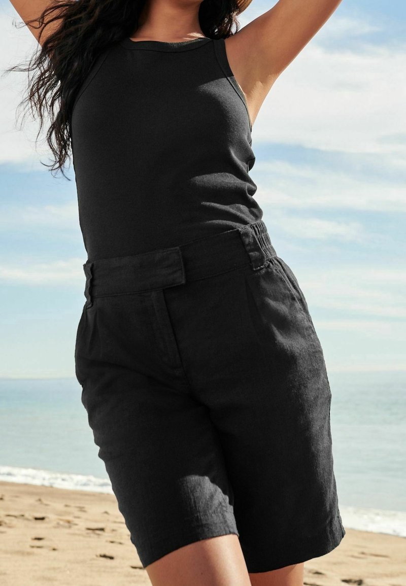 Schwarzes Tanktop mit rundem Ausschnitt, kombiniert mit hoch taillierten schwarzen Shorts mit texturierter Oberfläche und sichtbarem Taillendetail.