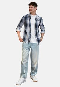 Jeansskjorte med blå og lysegrå mønstre, hvid T-shirt og lyseblå slidte jeans. Hvide sportssneakers fuldender looket.