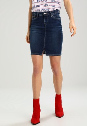 Kobieta ubrana w ciemnoniebieską mini spódnicę dżinsową z przednim rozcięciem, w połączeniu z czerwonymi botkami i białą bluzką z napisem "LEE JEANS".