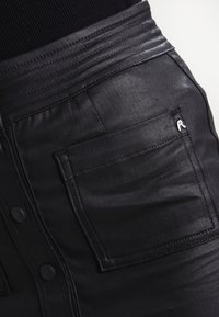 Czarne spodnie z ekologicznej skóry z teksturowanym paskiem w talii, przednią kieszenią oraz subtelnym detalem marki na kieszeni.