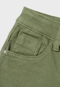 Tissu en denim vert olive présentant une poche arrière avec des coutures discrètes et un accent en métal, mettant en avant une finition texturée.