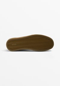 Schuhsohle aus glattem, tanfarbenem Gummi mit einem Zickzackmuster für besseren Halt. Flaches Design mit abgerundeten Kanten und geprägtem Branding.