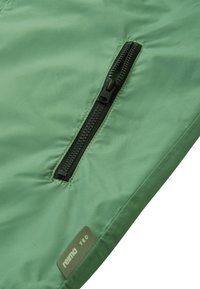 Green jacket fabric with a smooth texture and a vertical black zipper on the front. Notable brand tag visible near the hem.