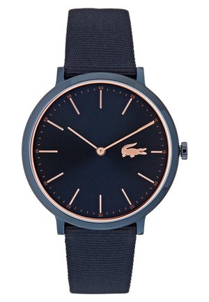 Cadran rond noir avec index et aiguilles en or rose, bracelet en tissu noir et logo crocodile en or rose à la position 3 heures.