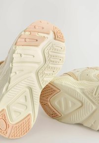 Lysfarvede træningssko med en tekstureret sål i beige og pink nuancer. Designet er struktureret med geometriske mønstre.
