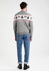 Grå stickad tröja med ett mönstrat ok som har julgranar och jultomtestans ansikten i röd och grön. Kombination med blå jeans och svarta stövlar.