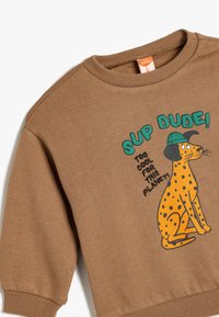 Bruine sweatshirt met een speelse illustratie van een geelgestippelde hond in een groene hoed, met de tekst "SUP DUDE! TOO COOL FOR THIS PLANET!"