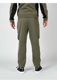 Pantalones de chándal verde oliva con puños elásticos y bolsillos laterales. Hechos de una tela suave, con acentos de paneles negros a lo largo de los lados.