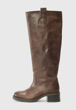 Brown leather knee-high boot with a rounded toe, block heel, and decorative tab at the top. Features a smooth, textured finish.