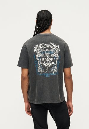 Person med fletninger iført en falmet sort T-shirt med detaljeret grafik og teksten "Replay Son of Temple" og "European Tour 1993" på ryggen.
