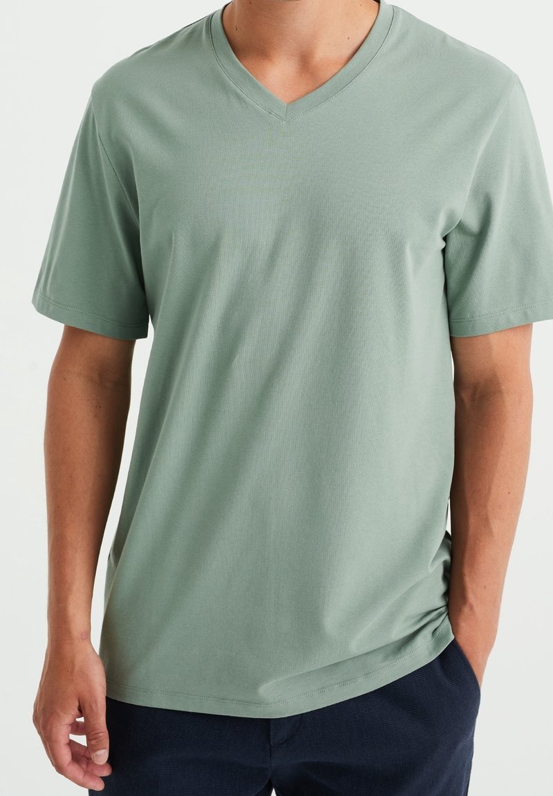 T-shirt vert clair à manches courtes et décolleté en V, fabriqué en tissu doux. Il présente une coupe décontractée et une texture lisse. Convient pour une tenue décontractée.