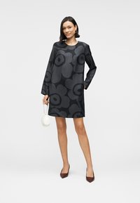 Μαύρο φόρεμα με λουλουδάτο μοτίβο, μακριά μανίκια, στρογγυλή λαιμόκοψη και χαλαρή εφαρμογή. Το ύφασμα έχει λεία υφή. Συνδυάζεται με μικρή λευκή τσάντα.