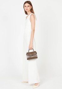 Sac à main en cuir marron avec une poignée supérieure, de forme rectangulaire et une fermeture magnétique, associé à une combinaison sans manches blanche et des chaussures beiges.