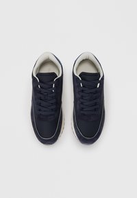 Navy blue sneakers with a mix of smooth and suede textures, rounded toe, lace-up design, and beige accents around the sole.