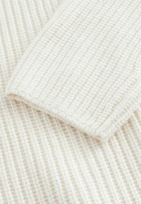 Gros plan d’un tissu tricoté blanc montrant des motifs détaillés en côtes texturées et point de semence.