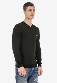 Schwarzer, langärmeliger V-Ausschnitt-Pullover aus weichem Material. Verfügt über ein kleines Logo auf der Brust und gerippte Bündchen für eine enganliegende Optik.