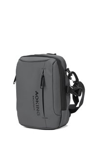 Zaino grigio realizzato in tessuto resistente, di forma rettangolare, con chiusura a zip, tracolla regolabile e testo di marca sul davanti.